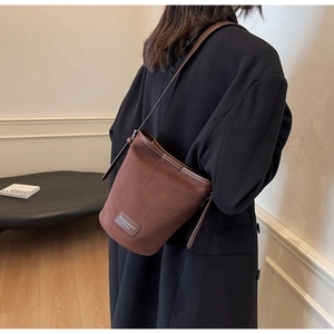 Nahaufnahme einer braunen Wildleder-Beuteltasche mit Lederriemen und Logo-Aufnäher