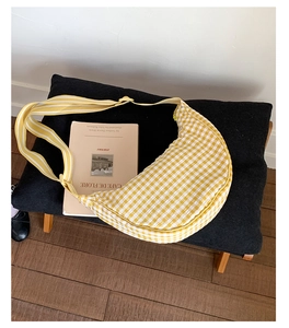 Detail view of yellow checkered crescent bag with striped strap on a vintage stool