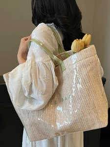 Large beige woven straw tote bag with green leather straps and THE BAG text print