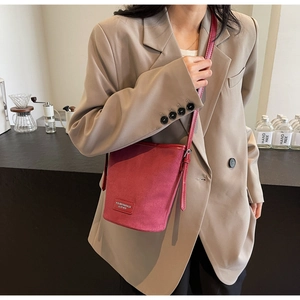 Detail der weinroten Matten Lederbeuteltasche mit Markenetikett und beigem Blazer
