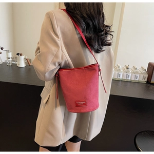 Detailansicht der tiefroten Eimer-Tasche aus Wildleder, von einem Model im Café getragen