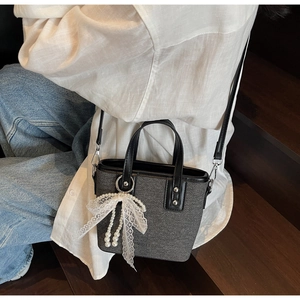Detail der grauen Tweed-Beuteltasche mit weißer Spitzenschleife und Perlenanhänger