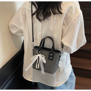 Detail der grauen Beuteltasche mit weißer Spitzenschleife und Perlenanhänger