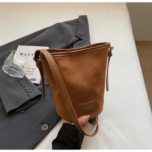 Detail der braunen Beuteltasche mit matter Wildledertextur und Leder Logo Aufnäher