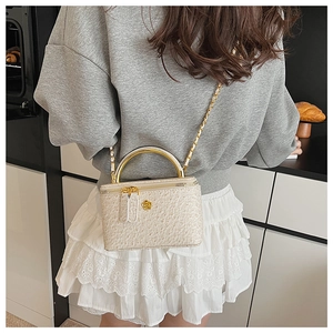 Chic beige box bag with ostrich texture, gold metal handle, and floral charm detail
