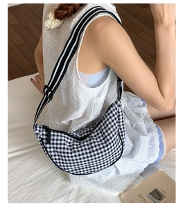 Detail of checkered dumpling bag with adjustable striped strap on a fashion model