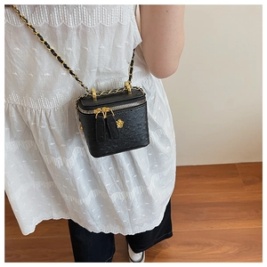 Detail view of black textured leather chain bag with golden camellia and double zippers