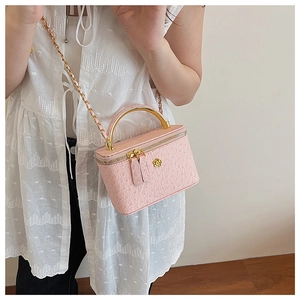 Detailed macro view of pink ostrich pattern vanity case with golden handle and chain strap