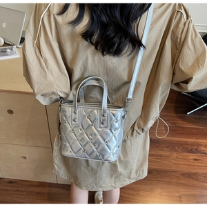 Upper body view of a silver quilted mini bucket bag with metallic studs on a shoulder strap
