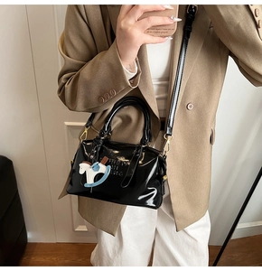 Gros plan d'un sac à main en cuir verni noir avec gaufrage et un charme de poney bleu