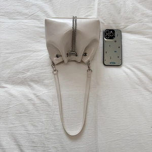 Top view of cream white patent leather bucket bag with silver chain and smartphone for size scale
