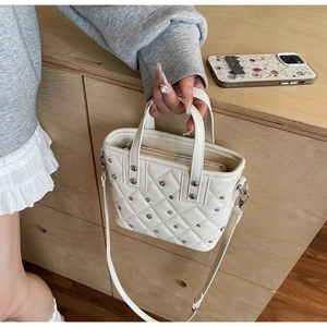 Close-up of white quilted bucket bag with silver rivet details and secure top zipper