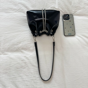 Macro view of glossy black patent leather bucket bag with silver chain and shoulder strap