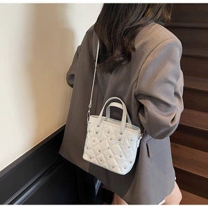 Detailed view of white quilted bucket bag with silver studs and elegant top handles