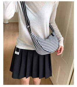 Detail view of black and white checkered dumpling bag with adjustable striped strap on model