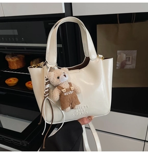 Detail view of cream bucket bag featuring teddy bear charm and textured oil wax finish