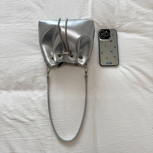 Detail view of silver metallic drawstring bucket bag with chain strap on white fabric