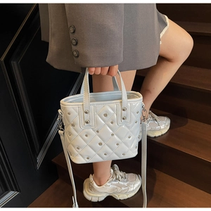 Detail of white quilted bucket bag with metal rivets and detachable shoulder strap