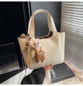 Detail of beige oil wax leather bucket bag with cute bear charm and embossed logo