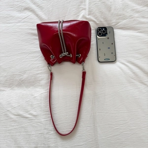 Detail view of red glossy bucket bag with silver drawstring chain and leather strap