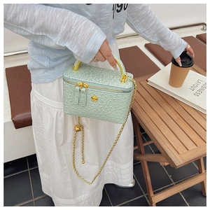 Detail of mint green box bag with ostrich texture and gold chain strap in outdoor setting