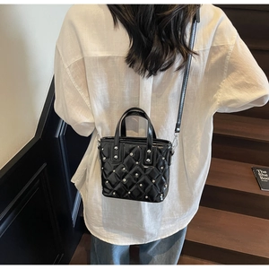 Lifestyle shot of black quilted bucket bag with silver studs on wooden stairs