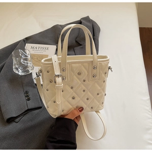 Close-up of cream quilted bucket bag with silver metal studs and thin shoulder strap