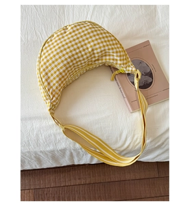 Close-up of yellow gingham crescent bag with adjustable striped strap on white fabric