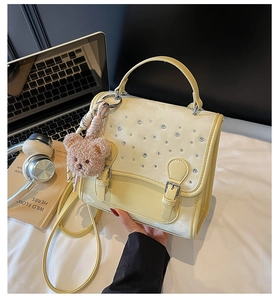 Detail view of cream-colored handbag with rhinestone accents and small teddy bear charm
