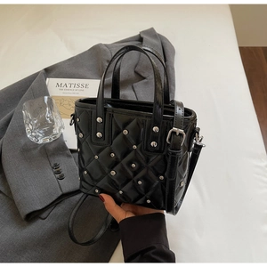 Detail of a black quilted mini tote bag featuring silver studs and a polished finish
