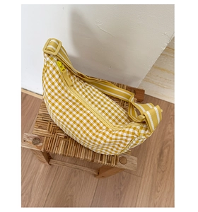 Detailed view of yellow and white checkered crescent bag on a vintage wooden stool