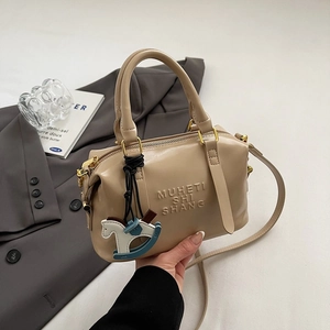 Gros plan du sac Boston beige avec lettrage embossé et charm de cheval en bois bleu