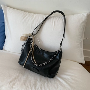 Detail of black lychee grain crescent tote with chain and bear charm on white bedding
