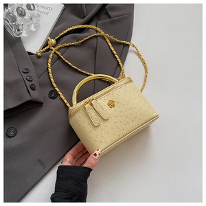 Close-up of beige ostrich texture leather bag with a gold flower clasp and metal handle