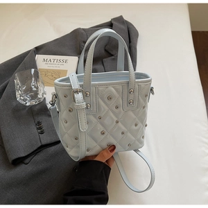 Detailed view of light blue quilted leather bucket bag with metallic rivet studs and strap