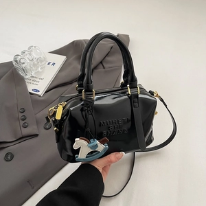 Gros plan détaillé du sac Boston noir brillant avec lettrage embossé et pendentif
