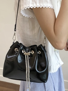 Minimalist black glossy bucket bag with silver chain drawstring shown in daily style