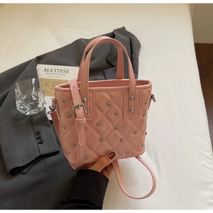 Pink quilted bucket bag with metal rivets, held in hand against an aesthetic background