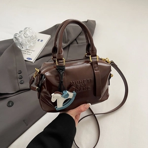 Sac Boston marron foncé avec lettrage embossé et breloque dans un cadre lifestyle