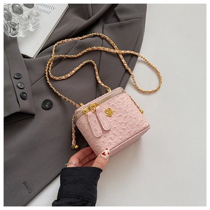 Detailed close-up of pink ostrich texture box bag with gold flower detail and chain strap