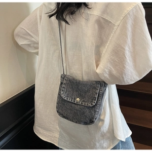 Detail of vintage washed denim crossbody bag with metallic button on model
