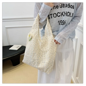 Detailed close-up of white lace tote bag featuring floral embroidery and daisy charm