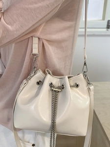 Minimalist white faux leather bucket bag with silver chain strap shown on a model