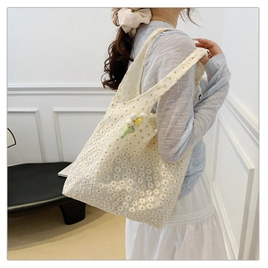 Detail of white lace crochet tote bag featuring daisy embroidery and floral pendant