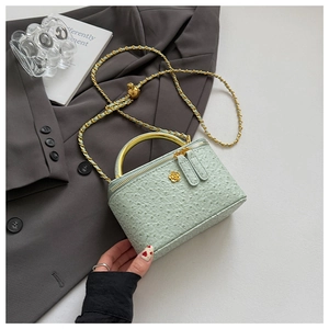 Detail of mint green box bag with ostrich texture, gold ring handle, and floral buckle