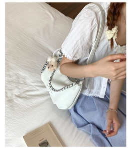 Detail of white leather shoulder bag with silver chain and cute teddy bear charm accessory