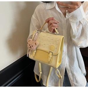 Detail of pale yellow mini backpack with scattered rhinestones and a brown teddy bear charm