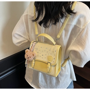 Detail view of yellow PU leather backpack with rhinestones and cute brown plush bear charm
