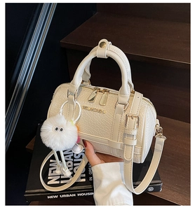 Detail of elegant beige crocodile-pattern handbag with fluffy pendant and gold hardware