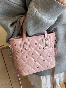 Pink quilted bucket bag with silver studs and crossbody strap shown with casual outfit